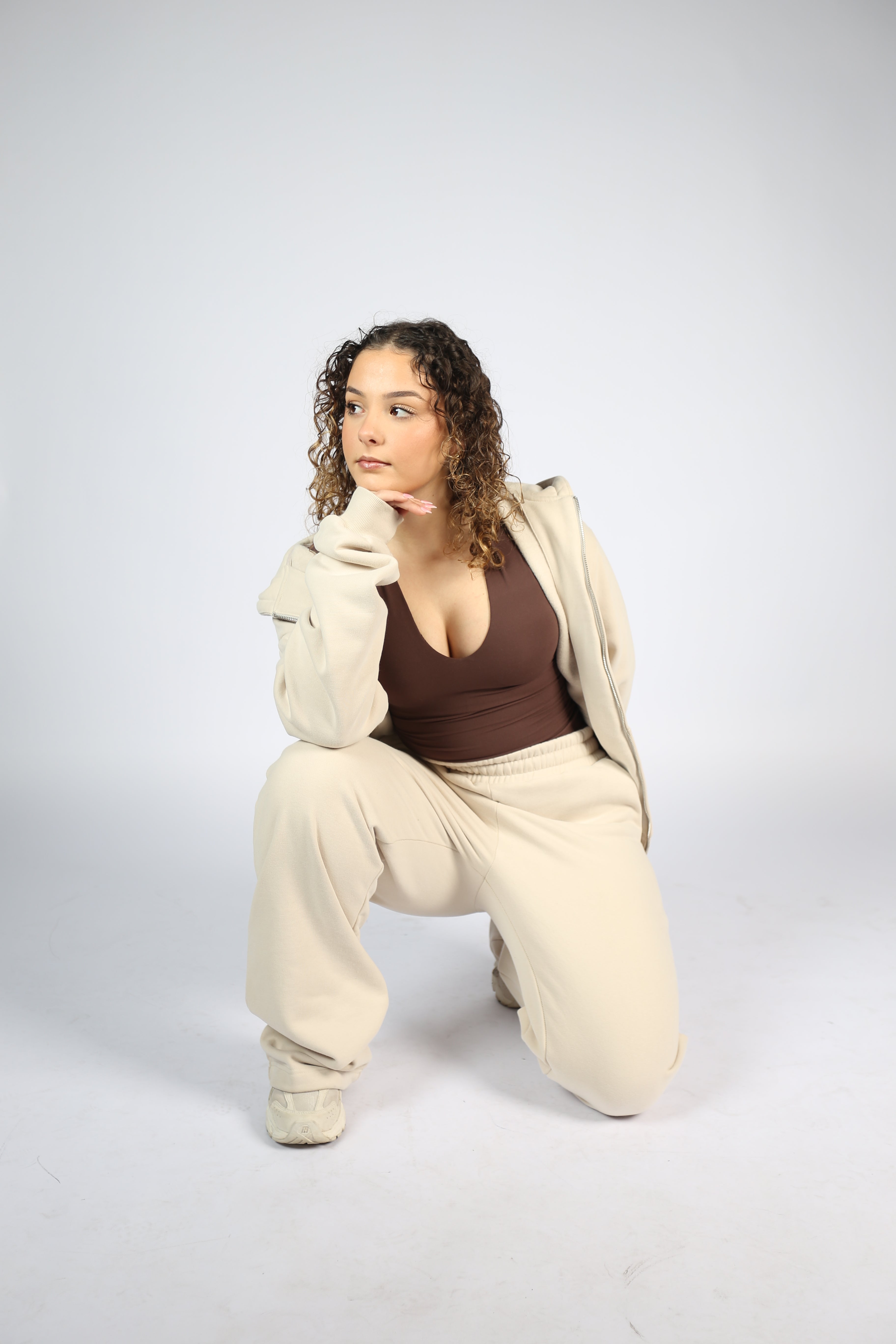 Person wearing a beige jacket and brown top on a white background